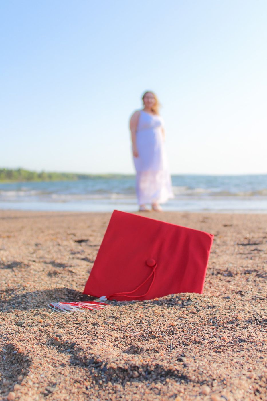 Graduation cap in the sand with the graduate standing at the water