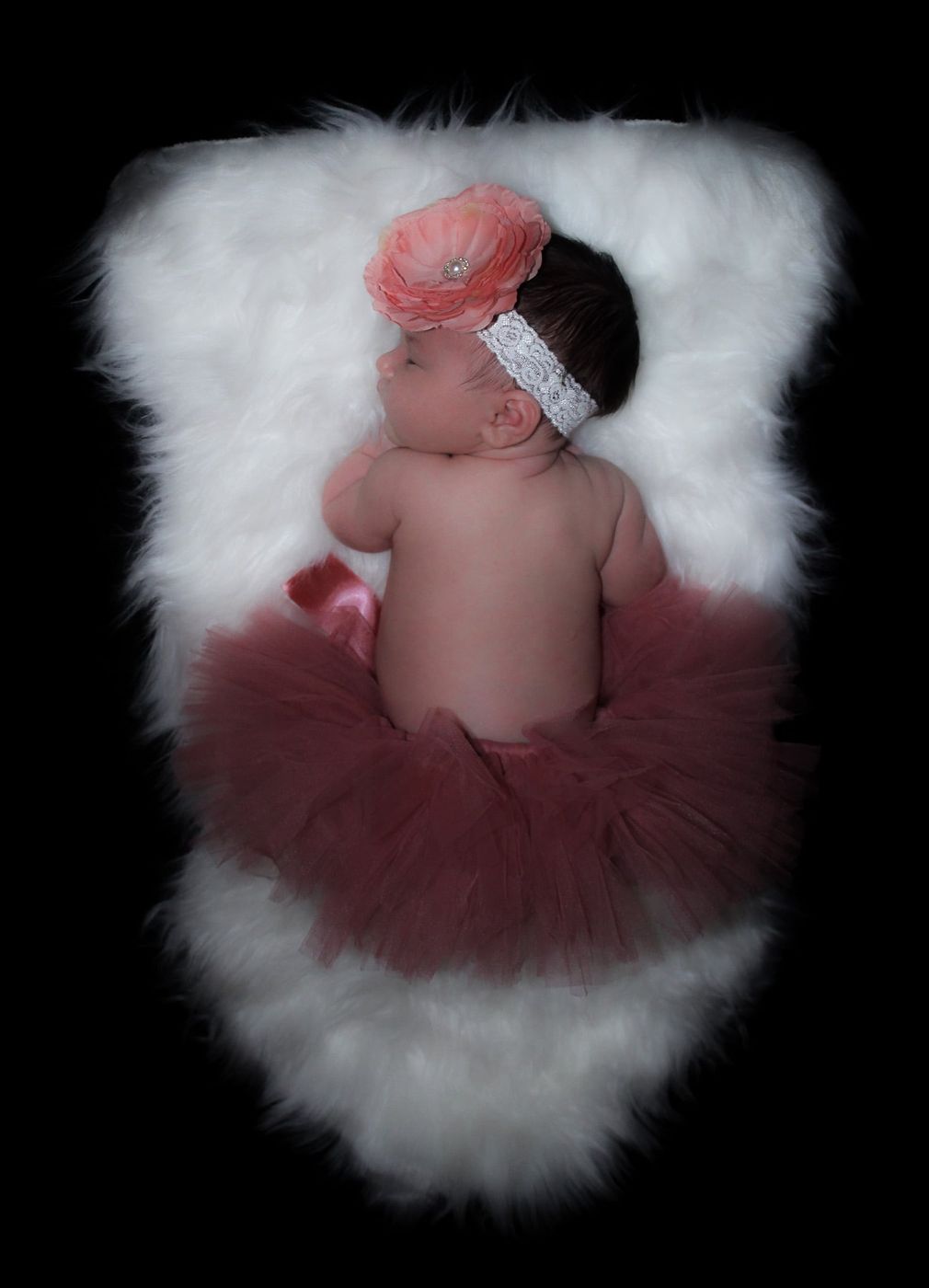 Newborn in a flower headband and tutu asleep on white fur