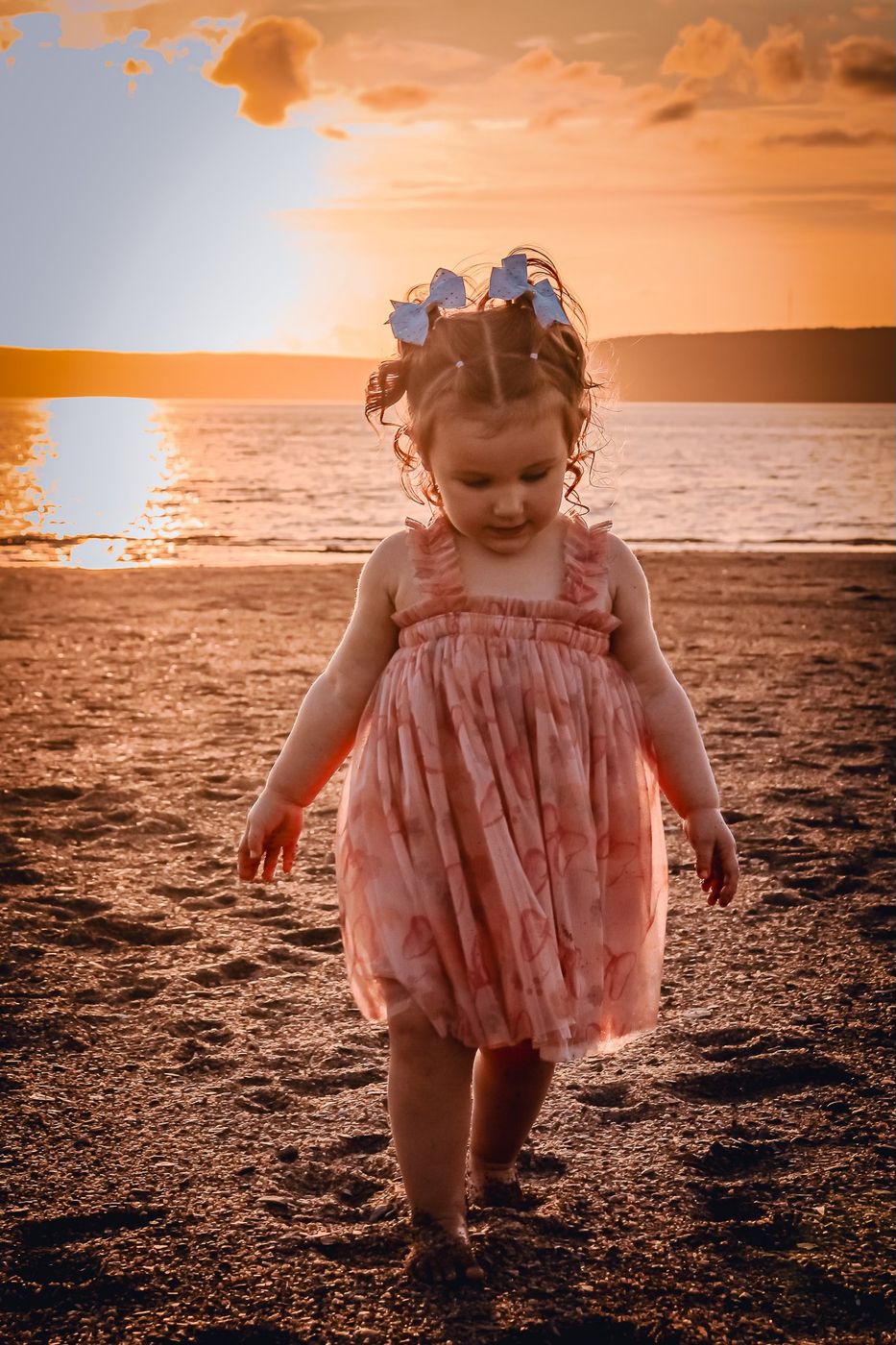 Toddler in a pink dress walking on the beach at sunset