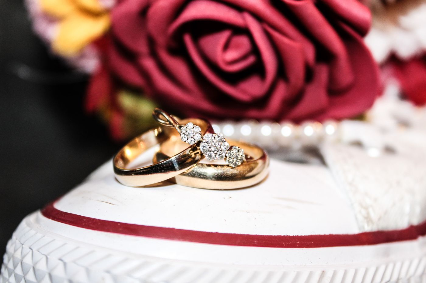 Wedding rings resting on a white sneaker beside a red rose